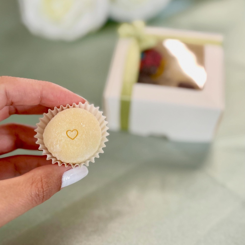 A single brigadeiro with a small heart stamp, held in hand in front of a ribboned gift box